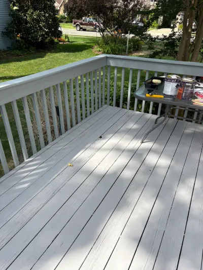 A deck mid-repaint in light grey, with paint supplies staged on a small table overlooking the front yard.