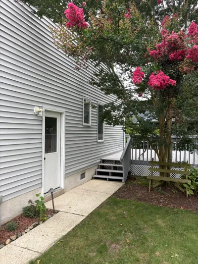 Side exterior of a house with grey siding, a wood deck, and a blooming pink crepe myrtle tree.