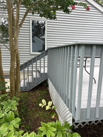 Exterior deck staircase with grey railings and white lattice skirting beside a vinyl-sided home.