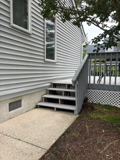 Side exterior of a house with vinyl siding, a wood deck staircase, and a concrete patio below.