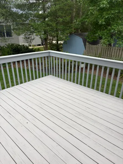 Weathered painted deck with peeling boards and railing overlooking a backyard with a shed.