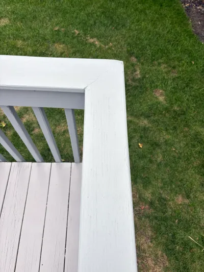 Close-up of a painted white deck railing corner above a lawn with patchy grass.