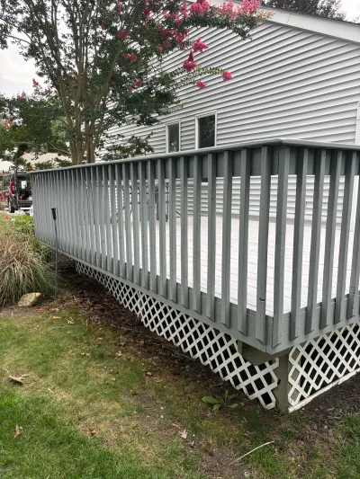 Grey painted deck with railing and white lattice skirting beside a house with vinyl siding.