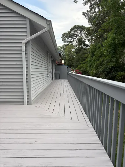 A long painted grey wood deck runs along the side of a house bordered by trees.