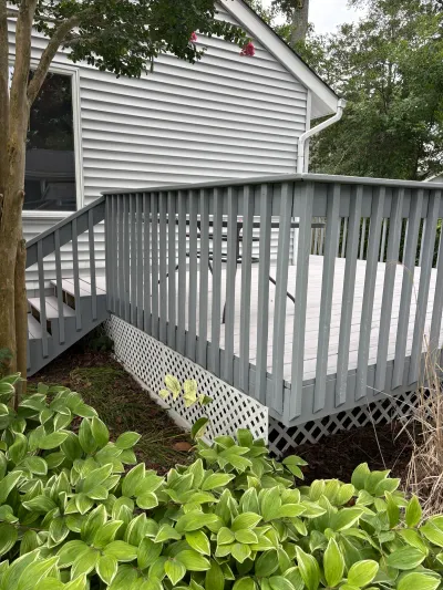 A grey painted wood deck with stairs and white lattice skirting attached to a house with vinyl siding.