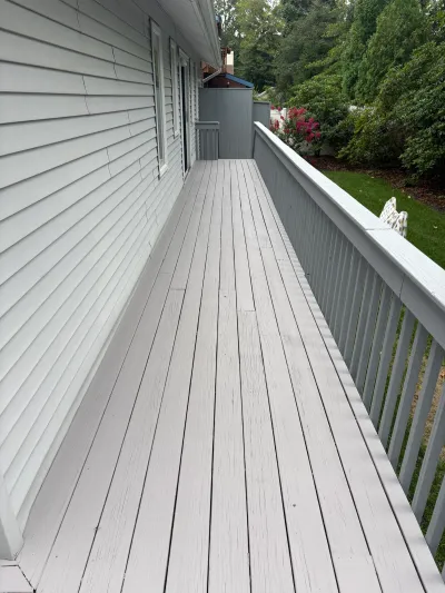 Long painted grey wood deck running alongside a house with a landscaped backyard view.