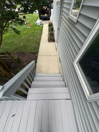 View down painted grey deck stairs beside a house with vinyl siding and a concrete walkway to the yard.