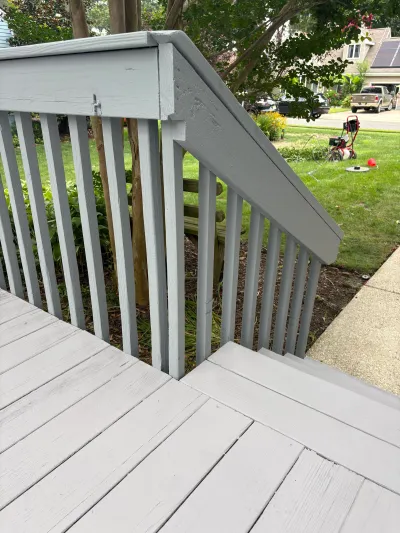Freshly painted grey wood deck railing and stairs leading down to a concrete walkway.