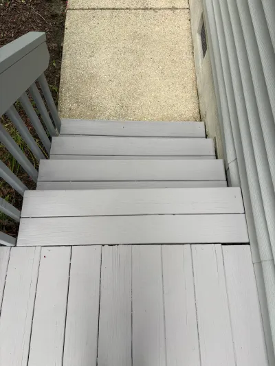 Painted grey wood deck stairs leading down to a concrete walkway beside a house.