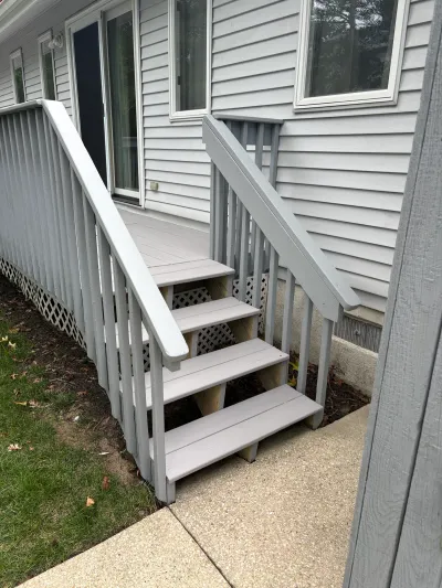 A painted grey wood staircase leads up to a sliding glass door on a light grey sided house.