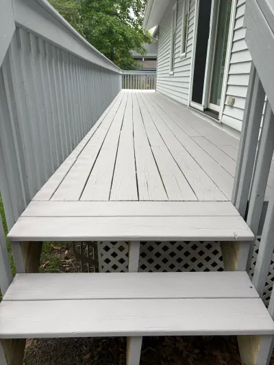 A weathered painted wood deck with cracking paint and stairs running alongside a house.