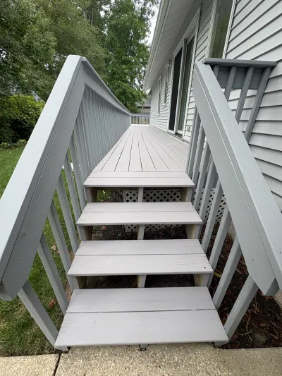 A grey-painted wood deck and staircase leading down to a concrete walkway beside a house.