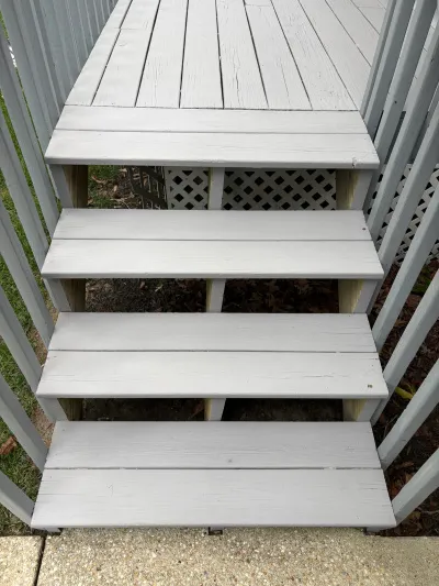 Weathered wooden deck stairs with peeling grey paint leading down to a concrete walkway.
