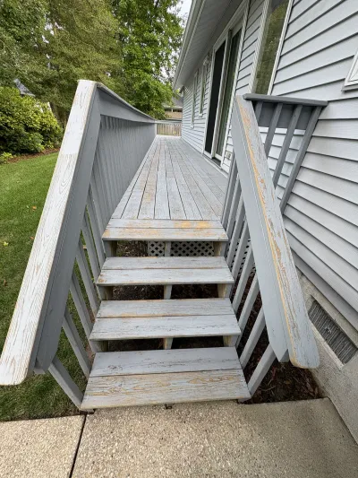 Weathered wood deck stairs with peeling paint alongside a house with vinyl siding.