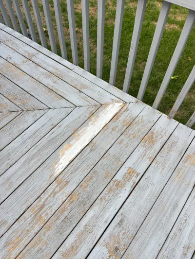 Weathered deck boards in a chevron pattern with heavily peeling grey paint, next to a painted railing and lawn.