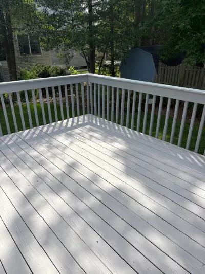 A white-railed painted wood deck overlooks a shaded backyard with a shed and picket fence.