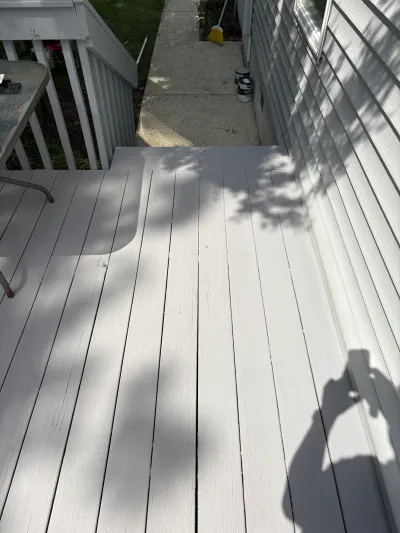 Freshly painted white deck boards leading to a concrete walkway beside a house with vinyl siding.
