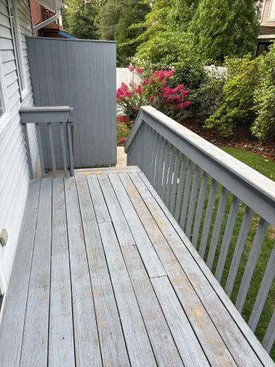 Weathered grey deck with peeling paint next to a tall utility enclosure and backyard landscaping.