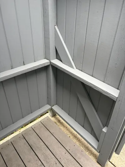 Close-up of a gray wood shed corner with a white diagonal brace, above composite decking.