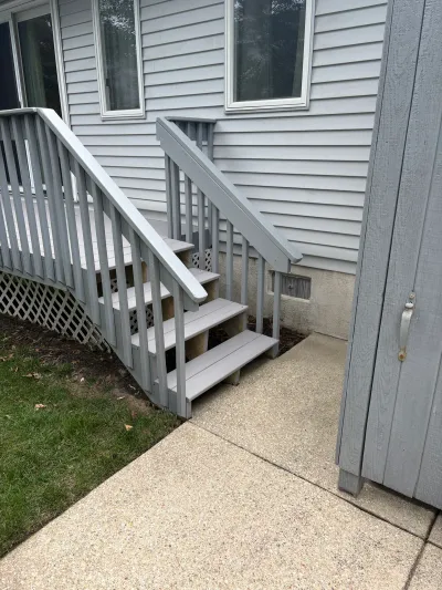 Grey painted deck stairs leading down to a concrete walkway beside a vinyl-sided house.