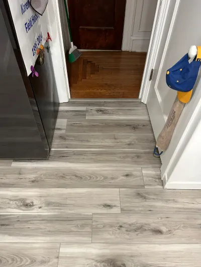 New grey wood-look vinyl plank flooring in a kitchen, transitioning to a dark hardwood hallway floor.