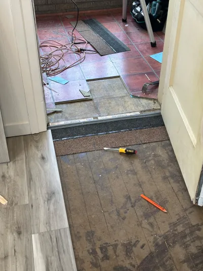 Flooring renovation in progress showing new plank flooring next to a room with tile being removed.