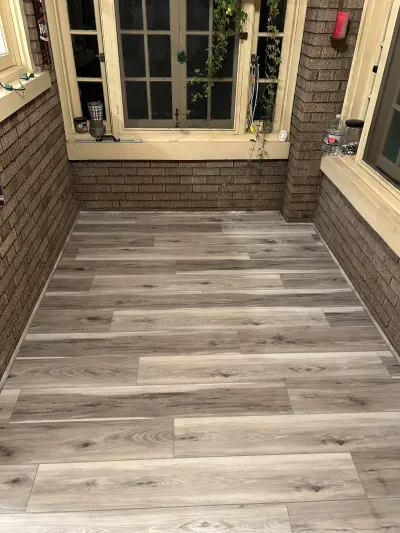 Enclosed brick sunroom with new wood-look tile flooring and a French door at night.