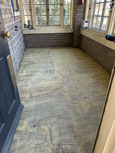 Worn vinyl flooring and exposed brick walls in a sunroom before renovation.