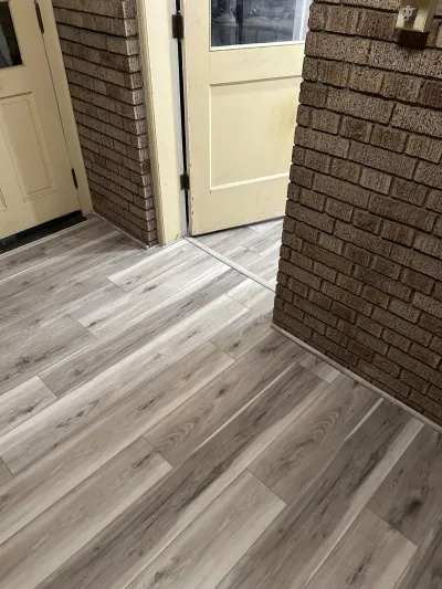 Entryway with wood-look vinyl plank flooring between brick columns and cream paneled doors.