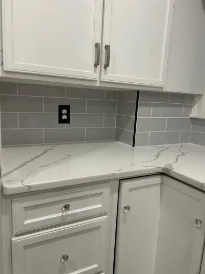 Close-up of a white kitchen corner with grey subway tile backsplash and veined quartz countertop.
