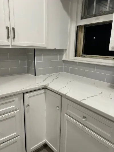 Kitchen counter with veined quartz countertop and partially installed grey subway tile backsplash near a window.
