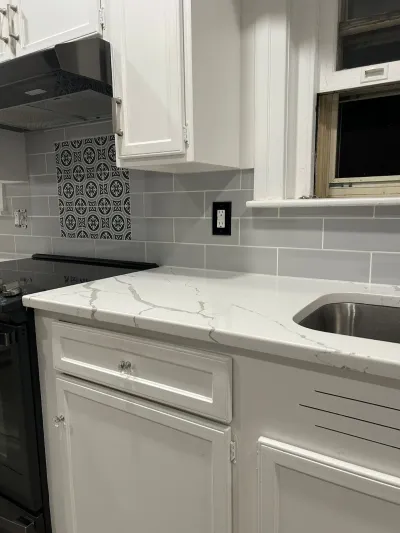 White quartz kitchen counter with grey subway tile backsplash and a patterned mosaic accent tile.