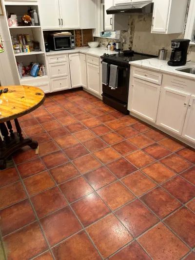 Kitchen before renovation with white cabinets, terracotta tile floor, and stripped backsplash wall.