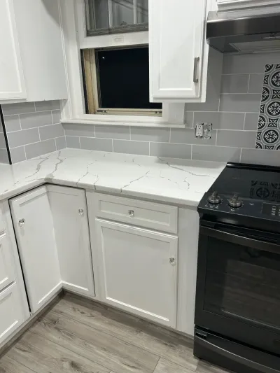 Finished kitchen corner with white cabinets, quartz counters, gray subway tile, and a black stainless range.