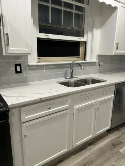 Finished kitchen sink area with white cabinets, quartz counters, and grey subway tile backsplash.