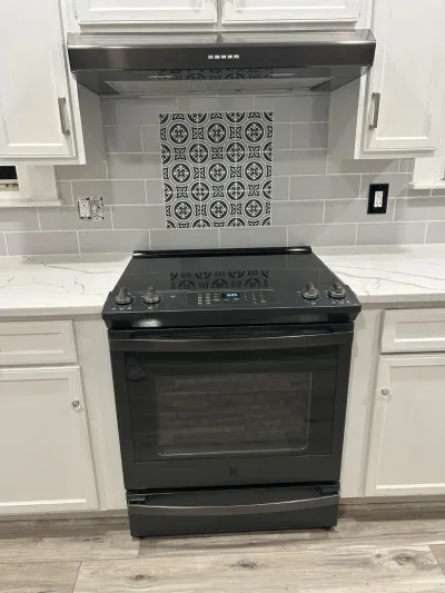 Kitchen range wall with black stainless stove, patterned tile accent, and white shaker cabinets.