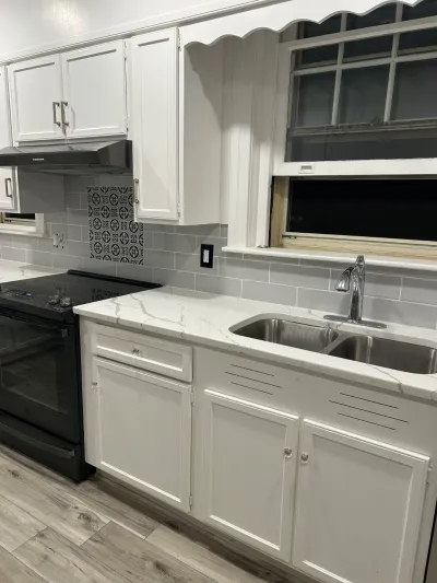Renovated kitchen with white cabinets, quartz counters, subway tile backsplash, and a black range.