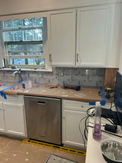 Kitchen mid-renovation with subway tile backsplash installation and protective coverings on counters.