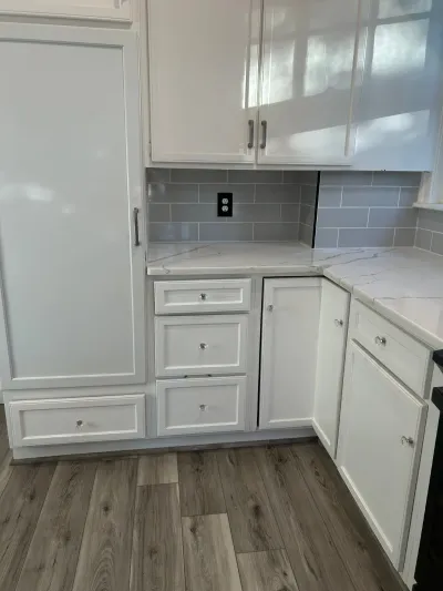 Corner of a white kitchen with quartz counters, grey subway tile backsplash, and wood-look flooring.