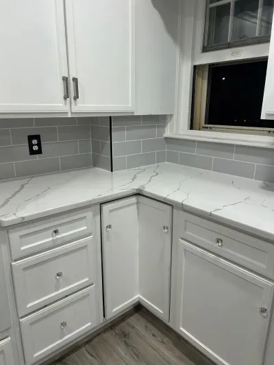 Corner of a white kitchen with quartz counters, grey subway tile backsplash, and glass cabinet knobs.
