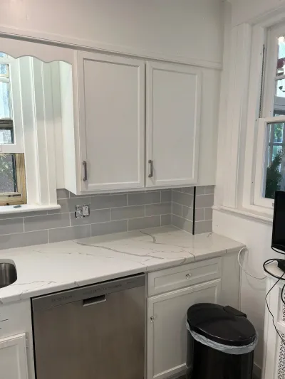 Renovated kitchen corner with white cabinets, quartz counters, and grey subway tile backsplash.