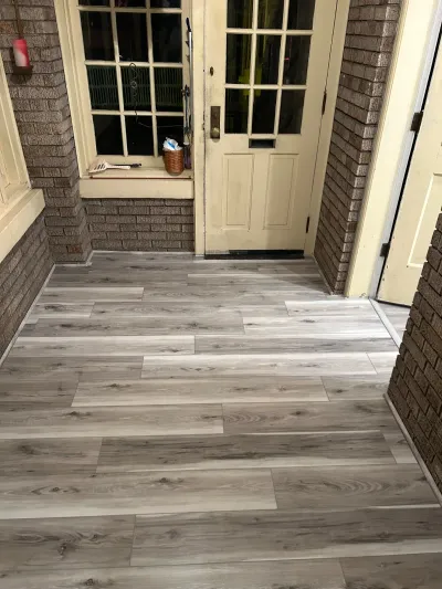 Newly installed gray wood-look vinyl plank flooring in a brick-walled entryway with a cream paneled door.