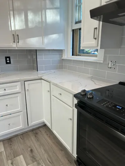 Corner of a white kitchen with grey subway tile backsplash, marble-look counters, and a black range.
