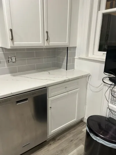 White shaker kitchen cabinets with quartz counters and grey subway tile backsplash above a stainless dishwasher.