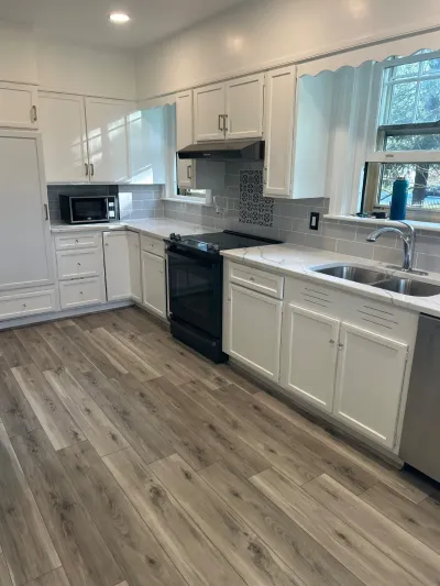 Renovated white kitchen with quartz counters, subway tile backsplash, and wood-look vinyl plank flooring.