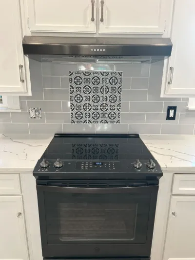 Kitchen range area with black stainless appliances, gray subway tile, and a patterned tile accent above the stove.