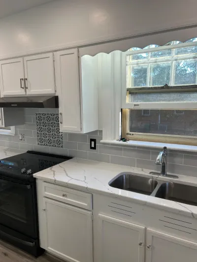 Bright white kitchen with quartz counters, gray subway tile backsplash, and a black range below a sunny window.
