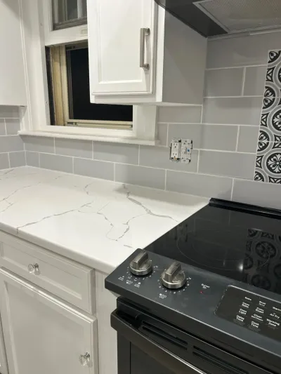 Kitchen counter and backsplash mid-renovation with quartz countertop, subway tile, and a black electric range.