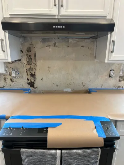 Kitchen backsplash removed down to bare wall, with countertop taped off during renovation work.