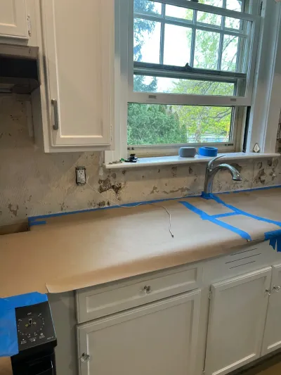 Kitchen mid-renovation with backsplash removed and countertop covered in protective paper and tape.